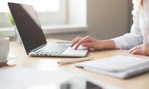 Mano su tastiera laptop, tazza caffè, quaderno. Ricerca su quanto guadagna un interprete per capire il potenziale di carriera.