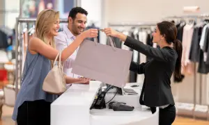 Una commessa sorridente consegna una borsa della spesa a una coppia felice in un negozio di abbigliamento.