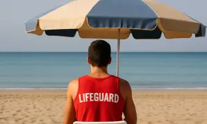 Ragazzo di 16 anni con maglietta "LIFEGUARD" sotto un ombrellone, ideale per lavori estivi.