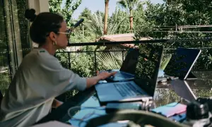 Donna lavora da remoto part time su un balcone lussureggiante, con laptop e tablet.