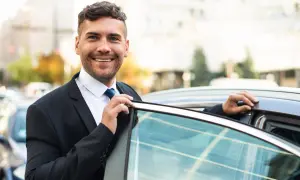 Un sorridente agente di commercio in giacca e cravatta apre la portiera di un'auto, pronto per un nuovo appuntamento.