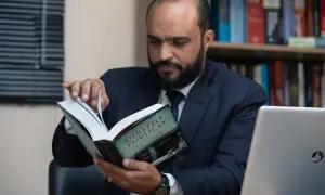 Uomo barbuto in giacca e cravatta legge un libro di diritto pubblico, forse cercando consigli su che liceo fare per diventare avvocato.