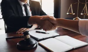 Avvocato stringe mano a cliente, con bilancia della giustizia e martelletto. Si discute quanto guadagna un avvocato civile.
