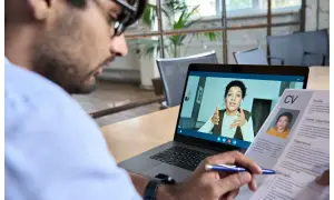 Uomo in videochiamata per un colloquio di lavoro da casa, con il suo CV aperto.
