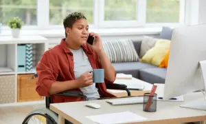 Persona in carrozzina al telefono, con tazza in mano, lavora da casa. Un esempio di inclusione per le categorie protette.