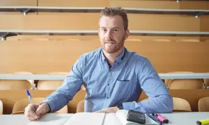 Uomo con barba rossa studia in aula, appunti e calcolatrice sul tavolo. Cosa studiare a 30 anni per trovare lavoro?