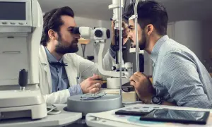 Un oculista esamina l'occhio di un paziente con uno strumento. Un percorso per diventare oculista inizia con un esame accurato.