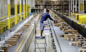 Un uomo lavora come corriere in un magazzino, sistemando pacchi su un nastro trasportatore pieno di scatole Amazon.