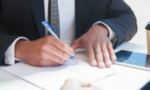 Un uomo in giacca e cravatta firma un documento, mostrando cosa fa un notaio: autentica e garantisce accordi legali con professionalità.