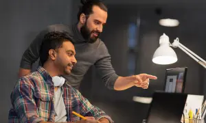 Due colleghi discutono un progetto al computer. Uno indica lo schermo, l'altro ascolta. Forse stanno valutando il project manager stipendio netto.