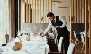 Cameriere in elegante divisa prepara la sala per la cena, un esempio di vitto e alloggio curato nei dettagli.