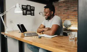 Giovane uomo sorride mentre lavora al computer, un esempio di **lavori online per studenti** da casa.
