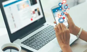 Gestione social media: un lavoro che può portare a un ottimo stipendio. La persona interagisce con notifiche e like su uno smartphone, accanto a un laptop aperto.