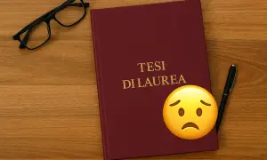 Tesi di laurea e-campus, occhiali e penna su un tavolo di legno. Un emoji triste accanto al titolo.