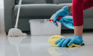 Mani guantate spruzzano detergente e puliscono il pavimento. Inizia il lavoro pulizie mattina con un panno giallo e uno straccio sullo sfondo.