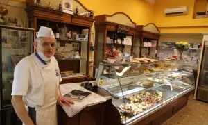 Pasticcere esperto, con vitto e alloggio, mostra la sua vetrina piena di dolci.