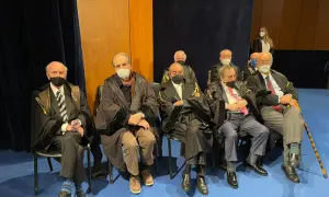 Uomini in toga seduti, alcuni con mascherina. Un uomo anziano potrebbe diventare avvocato a 50 anni, dimostrando che non è mai troppo tardi.