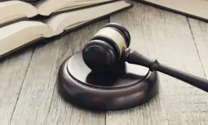 Martelletto da giudice su tavola di legno, con libri aperti sullo sfondo. Simbolo di giustizia e di studi di scienze giuridiche Pegaso.