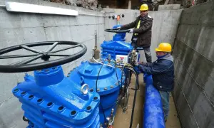 Lavoratori con elmetti gialli operano su grandi valvole blu di un acquedotto. Previste 200 assunzioni per il lavoro acquedotto pugliese.