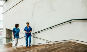 Due fisioterapiste in camice blu discutono sulle scale, forse valutando nuove offerte lavoro fisioterapista.
