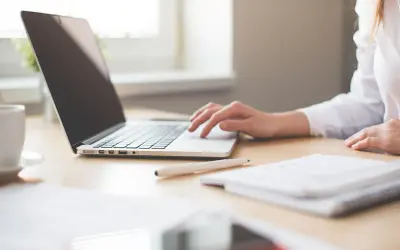 Mano su tastiera laptop, tazza caffè, quaderno. Ricerca su quanto guadagna un interprete per capire il potenziale di carriera.