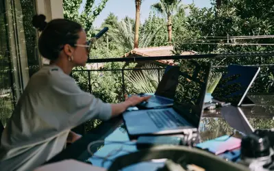 Donna lavora da remoto part time su un balcone lussureggiante, con laptop e tablet.
