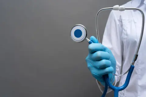Mano con guanto blu tiene uno stetoscopio, simbolo del piano di studi medicina San Raffaele.