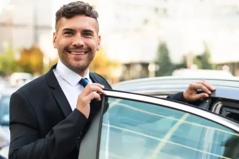 Un sorridente agente di commercio in giacca e cravatta apre la portiera di un'auto, pronto per un nuovo appuntamento.