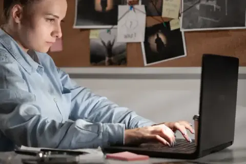 Giovane donna analizza prove su un laptop, un'indagine di criminologia a Milano.