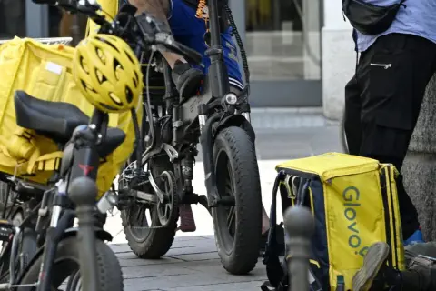 Corrieri Glovo con borse gialle e biciclette elettriche, pronti a lavorare.