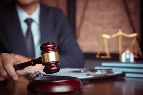 Giudice con martelletto, bilancia della giustizia e casa in miniatura. Un futuro master criminologia pegaso potrebbe studiare questo caso.