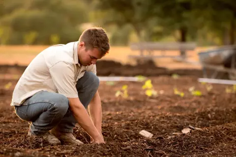 Un operaio di produzione si inginocchia in un campo, lavorando la terra con cura.