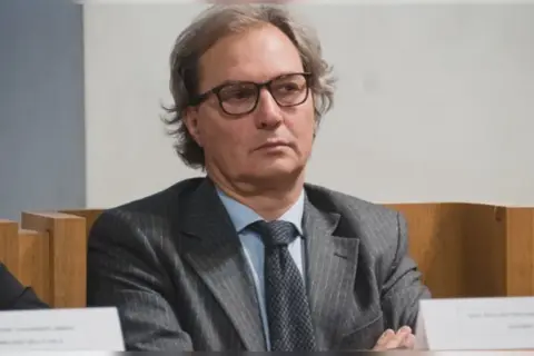 Uomo con occhiali, abito gessato e cravatta scura. Un procuratore cosa fa? Si occupa di giustizia e indagini.