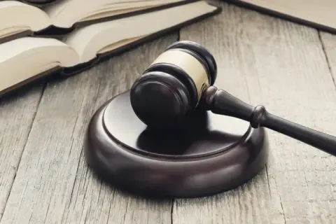 Martelletto da giudice su tavola di legno, con libri aperti sullo sfondo. Simbolo di giustizia e di studi di scienze giuridiche Pegaso.
