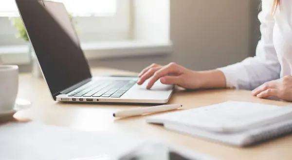 Mano su tastiera laptop, tazza caffè, quaderno. Ricerca su quanto guadagna un interprete per capire il potenziale di carriera.