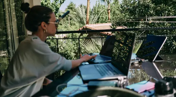 Donna lavora da remoto part time su un balcone lussureggiante, con laptop e tablet.