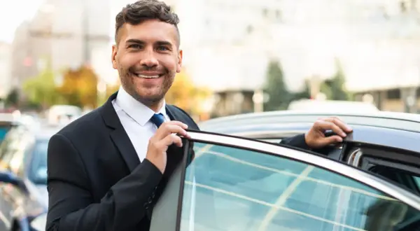 Un sorridente agente di commercio in giacca e cravatta apre la portiera di un'auto, pronto per un nuovo appuntamento.