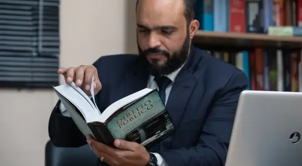Uomo barbuto in giacca e cravatta legge un libro di diritto pubblico, forse cercando consigli su che liceo fare per diventare avvocato.