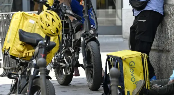 Corrieri Glovo con borse gialle e biciclette elettriche, pronti a lavorare.