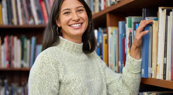 Sorriso sereno mentre sceglie un libro, immersa nell'atmosfera di chi ama lavorare in biblioteca.