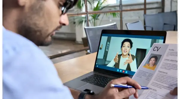 Uomo in videochiamata per un colloquio di lavoro da casa, con il suo CV aperto.