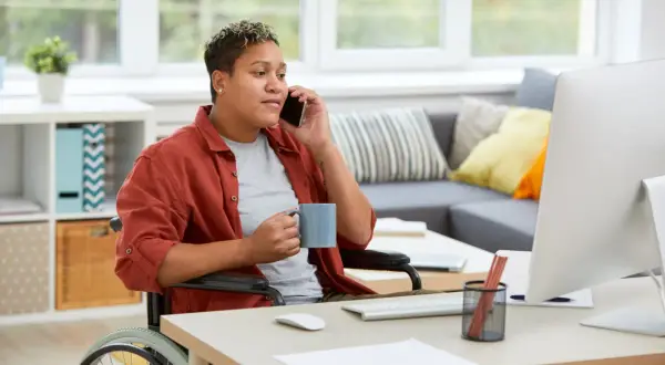 Persona in carrozzina al telefono, con tazza in mano, lavora da casa. Un esempio di inclusione per le categorie protette.