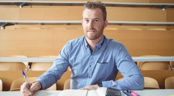 Uomo con barba rossa studia in aula, appunti e calcolatrice sul tavolo. Cosa studiare a 30 anni per trovare lavoro?