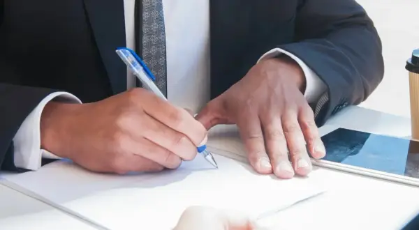 Un uomo in giacca e cravatta firma un documento, mostrando cosa fa un notaio: autentica e garantisce accordi legali con professionalità.