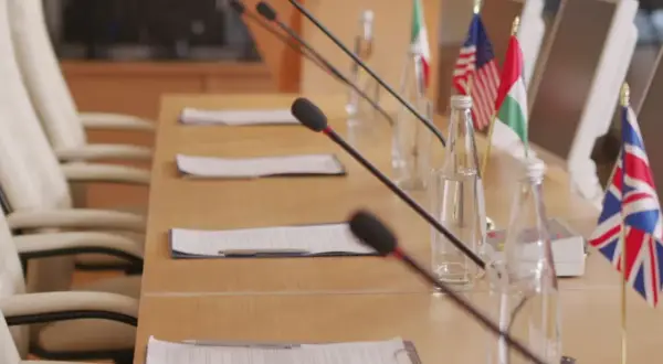 Tavolo da conferenza con microfoni, bandiere di diverse nazioni e fogli. Forse qui si discute come si diventa console.