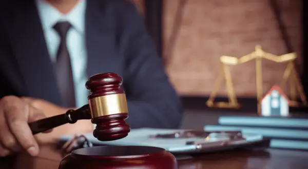 Giudice con martelletto, bilancia della giustizia e casa in miniatura. Un futuro master criminologia pegaso potrebbe studiare questo caso.