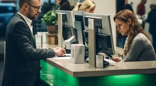 Uomo in giacca e donna al bancone di una banca, concentrati sul lavoro. Per lavorare in banca serve la laurea, e loro sembrano averla.