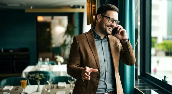 Un uomo sorride al telefono, un esempio di come un **innovation manager cosa fa**: gestisce idee e progetti con entusiasmo, in un ambiente moderno.