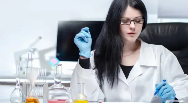 Ingegnere biomedico al lavoro in laboratorio, con provette e becher pieni di liquidi colorati.