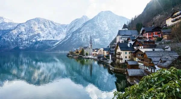 Villaggio alpino con case in legno sul lago, montagne innevate sullo sfondo. Ideale per offerte di lavoro stagione invernale vitto e alloggio.